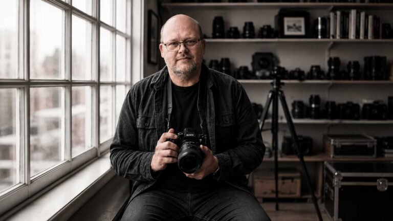 Fotograf mit Kamera in einem Studio mit Objektiven und Fotoausrüstung im Hintergrund