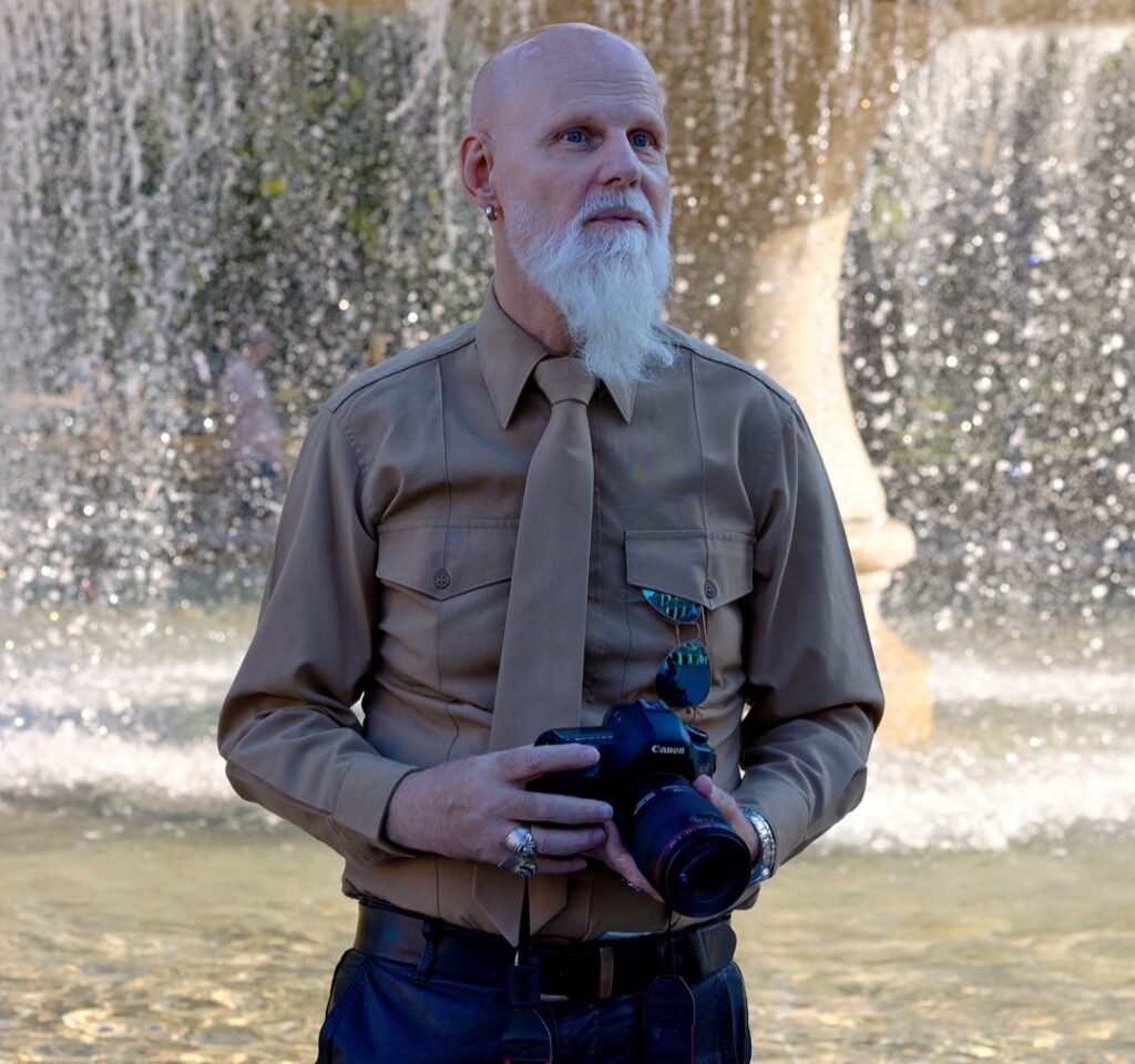 Klaus steht mit einer Canon Kamera vor einem Brunnen an der Konstablerwache in Frankfurt.